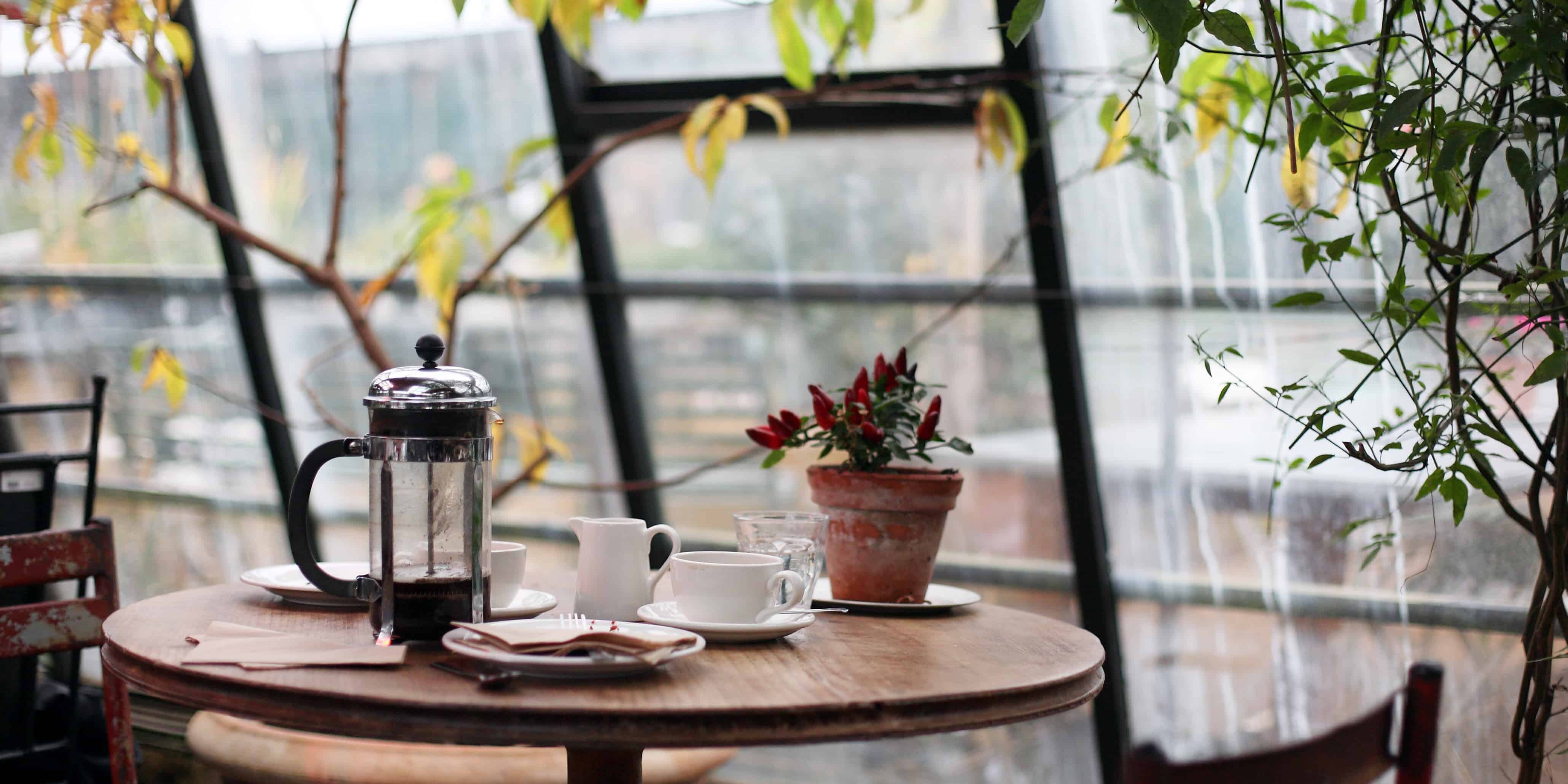round brown wooden table with french press on top with white ceramic teacup beside