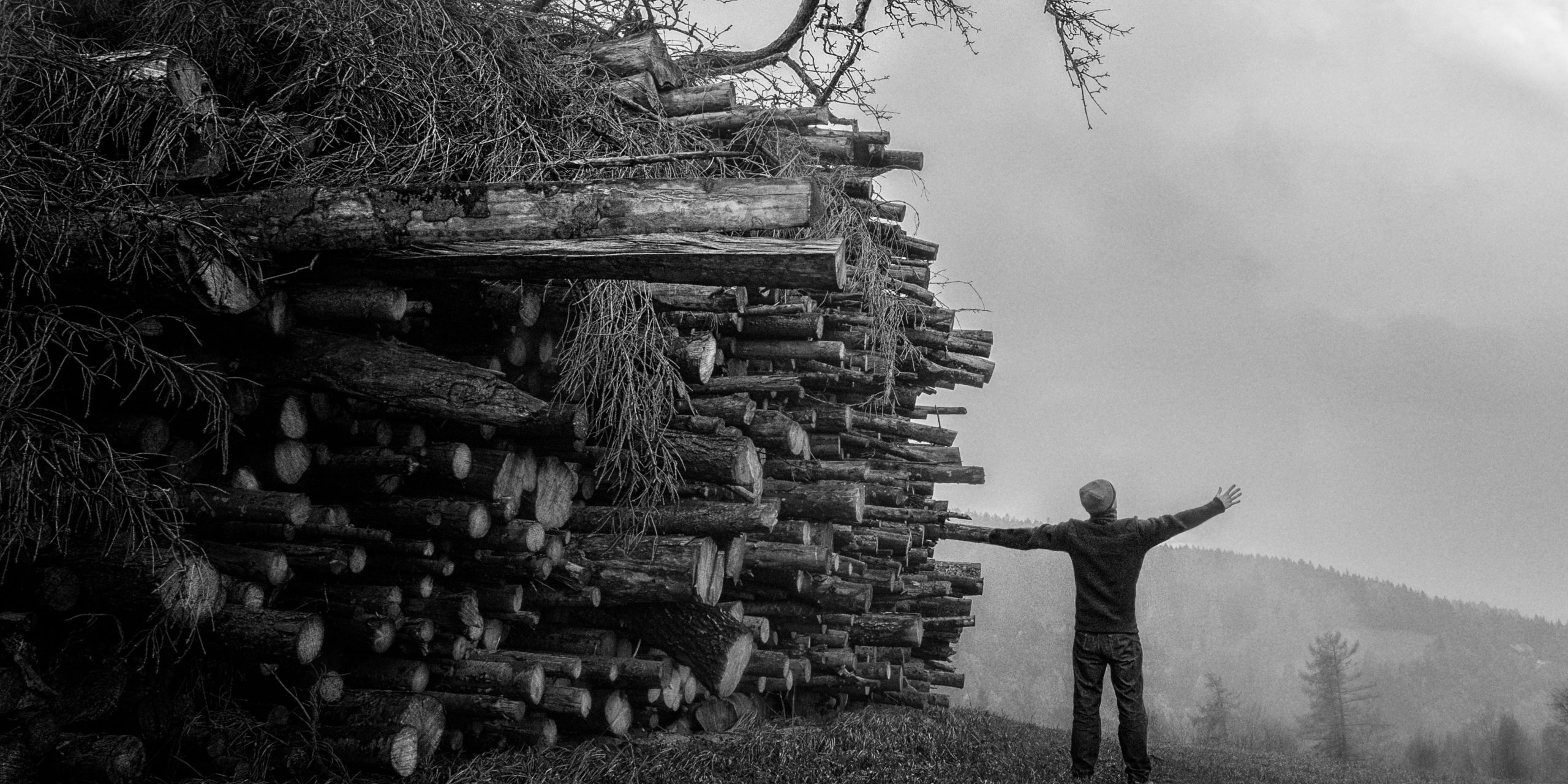 grayscale photography of man standing next to piles of woods